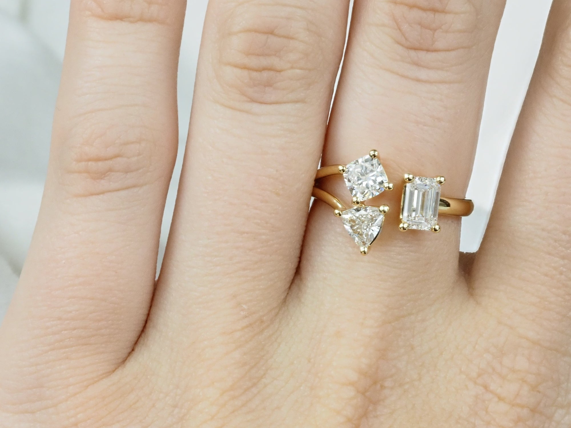 Gold ring with three diamond stones on a hand against a neutral background